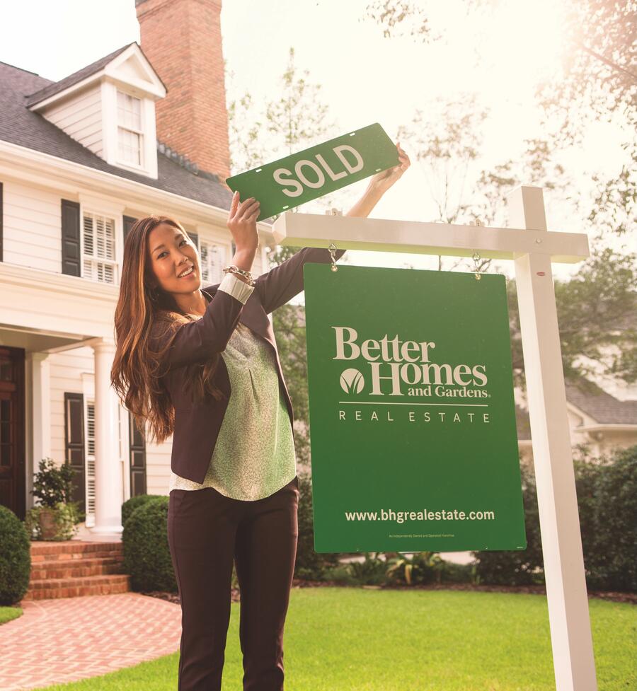 A Better Homes and Gardens Real Estate agent placing a SOLD rider on a yard sign